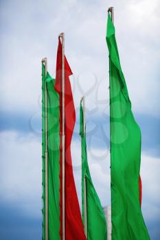 Flagpoles with vertical green and red flags against a blue sky. Vertical shot.
