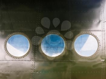 Portholes on military green painted metal background with rivet. Three portholes on board old retro airplane. Outside view of the old aircraft.