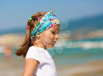 Profile of baby girl with a bandanna on his head on a blurred background of blue sky and sea. Hot sunny summer day. Selective focus.