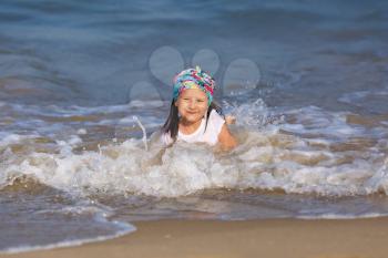 Smiling child in a white t-shirt lying in water on the beach on a clear sunny day. Shallow depth of field. Focus on the model's face.