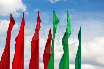 Several flagpoles with vertical green and red flag against a blue sky.