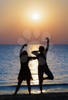 Two girls dancing at sunset on a background of the sea. Focus on models. Shallow depth of field. Toned image.