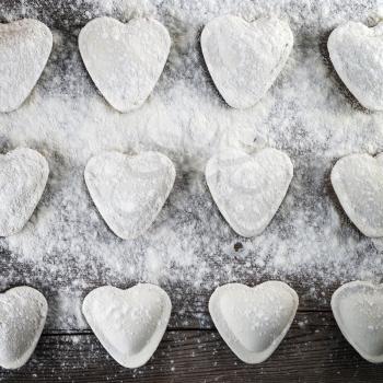 Cooking ravioli. Heart shaped dumplings, flour and rolling pin on wooden background. Top view.
