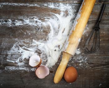 Eggs, eggshells, flour and rolling pin on wooden background. Vintage cooking background.