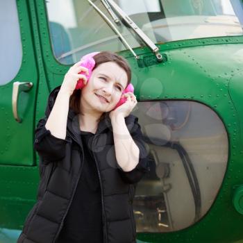 Woman listening to music with pink fur headphones over green helicopter cabin