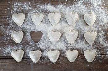 Heart shaped ravioli sprinkle with flour, on wooden background. Uncooked ravioli hearts. Cooking dumplings. Top view.