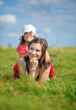 Mother and her little daughter enjoying a sunny summer day lying on green grass. Shallow depth of field. Selective focus on mother's face. Vertical shot.