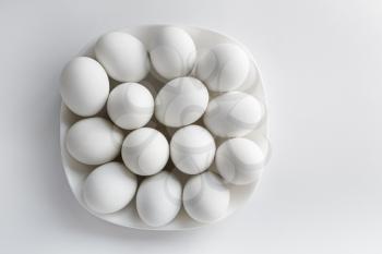 White eggs on a white square plate on a light background. Space for text. Top view.