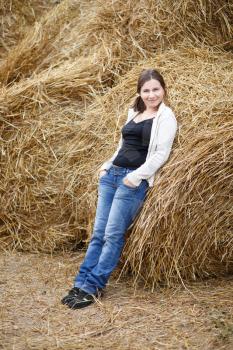 Pretty young woman in a white blouse and jeans posing on the background of haystacks.