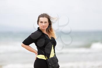 Pretty young woman looking at the camera, posing on a blurred background of ocean waves. Shallow depth of field. Focus on model.