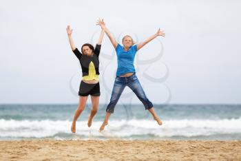 Two happy girls jumping on the beach against the sea and cloudless sky. Shallow depth of field. Focus on the model.
