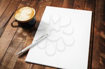 Blank letterhead, coffee cup and pen on vintage wooden table background. Blank branding template. Photo of blank stationery. Mock-up for design portfolios.