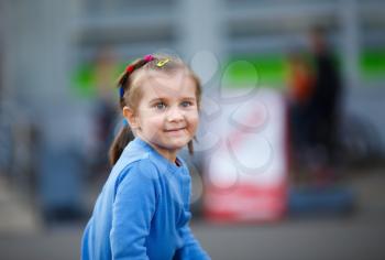 Portrait of a child in blue jacket against blurred street background. Little girl outdoors. Shallow depth of field. Selective focus.