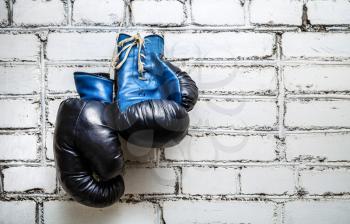 Pair of old blue boxing gloves hanging on white brick wall background.