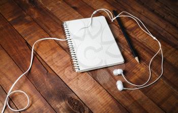 Blank notebook, pencil and headphones on wooden table background. Blank paperwork template for design portfolios.