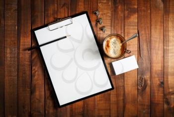 Blank paperwork template for designers. Responsive design mockup on vintage wooden background. Blank paper, letterhead, coffee cup, business cards and pencil on wooden table background. Top view.