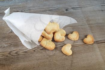 Delicious sweet cookies in the form of hearts in a paper wrapper on a wooden background.