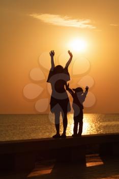 Mom and little daughter with their hands up to meet the sunrise over the sea. Silhouettes of women and girl. Toned image.