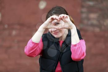 Pretty young woman making a heart gesture with her hands. Girl shows the heart with his hands. Shallow depth of field. Selective focus on the model's face.