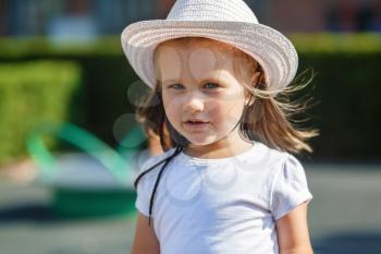 A child with long hair in white hat and t-shirt. Clear sunny summer day. Shallow depth of field. Selective focus on the model's face.