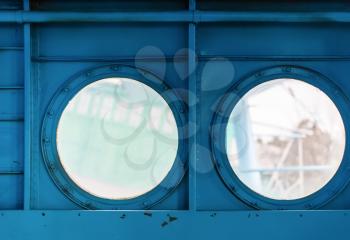 Two metal portholes with bolts on painted blue metal background. Inside view of the old aircraft.