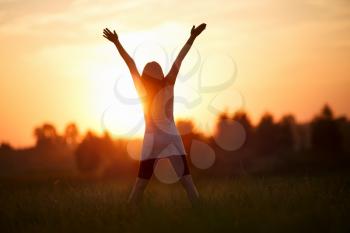Woman with arms raised looking at the sun. Focus on model. Shallow depth of field.