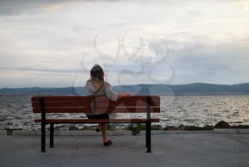 A woman sitting on a bench in the early morning and admire views of the bay and mountains. View from the back. Shallow depth of field. Focus on model.