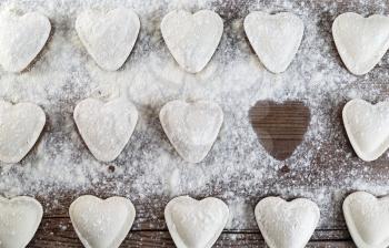 Heart-shaped ravioli sprinkled with flour on a wooden tabletop. Cooking dumplings. Top view