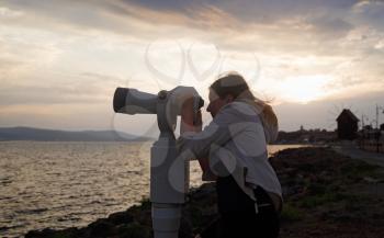 A woman using sea binocular working with coins against the background of a sea landscape in the early morning. Sunrise in the background. Shallow depth of field. Focus on the model.