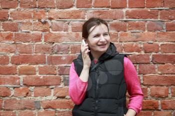 Smiling woman talking on a mobile phone against the backdrop of an old brick wall.