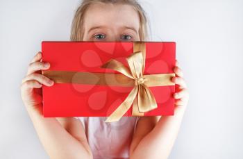 Red gift box with golden ribbon and bow in the hands of a child.