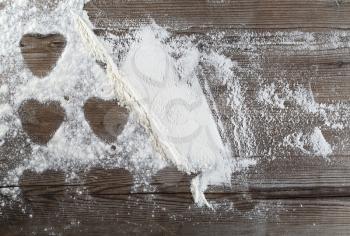 Flour sprinkled on a wooden table, with traces of cookies in the form of hearts. Culinary background. Top view.