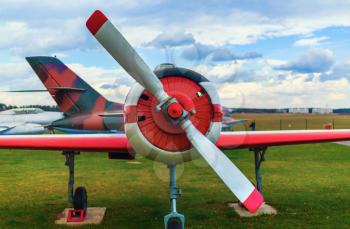 Front view of the part of the fuselage of the old military single-engine plane with a propeller. The airplane parked on the green grass. Selective focus on propeller.