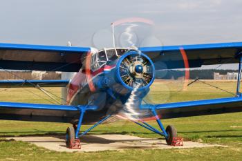 Old bright blue airplane with a rotating propeller close-up. Front view. Clear sunny day.