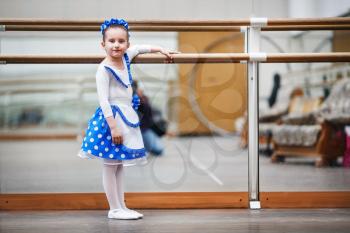 Child girl at a ballet school. Little girl ballerina posing at ballet barre. Happy girl in a dance class. Shallow depth of field. Selective focus.