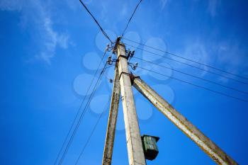 Concrete pillar with electric wires and a birdhouse on bright blue sky background.