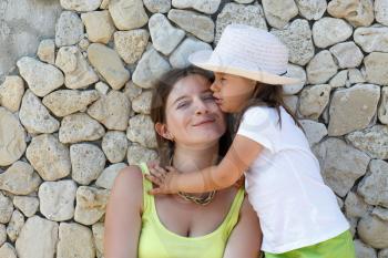 Portrait of mother and daughter. Smiling young woman and child on the background of an old stone wall.