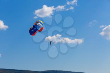 Parachutist on colorful parachute in a clear blue sky with a few clouds.