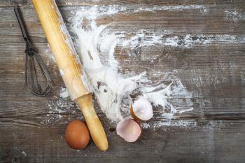 Eggs, eggshells, flour and rolling pin on wooden background. Top view.
