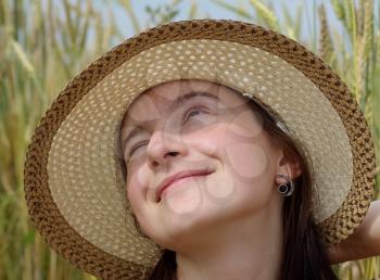 Pretty young woman in a straw hat smiling and squinting in the bright sun and looking up. Close-up portrait of a girl.
