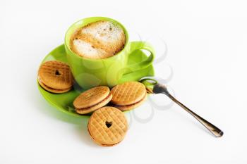 Coffee with foam in a green cup, saucer, spoon and tasty cookies.