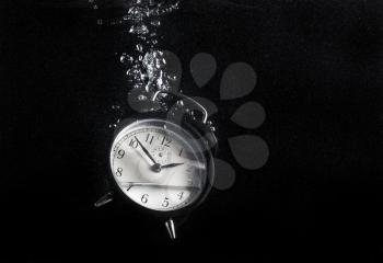 Concept of time. Vintage alarm clock in water with air bubbles. Photo on black background. Space for text. High speed photography.