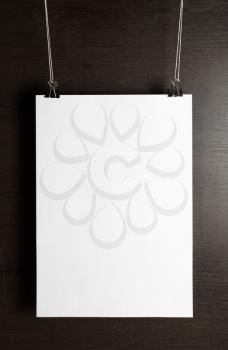 Blank white paper poster hanging on dark wooden background. Front view.