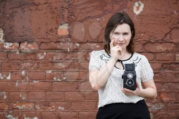 Portrait of a pretty young woman photographer with retro camera in hand. Old brown vintage grunge wall in the background.
