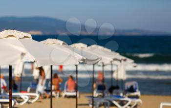 White beach umbrellas on a blurred background of blue sea and the mountains. White parasols. Blurred beach background. Shallow depth of field. Selective focus.