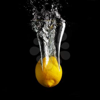 Fresh yellow lemon falling into the water with a splash and air bubbles. Healthy food on black background. Wash fruits.