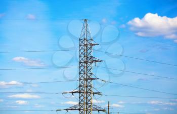 Electricity transmission pylon against blue sky with white tiny clouds. High voltage tower.