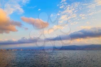 Beautiful morning seascape. Bright blue sky with cumulus clouds and a calm sea. The mountains and the city on the horizon. Dawn above the sea.