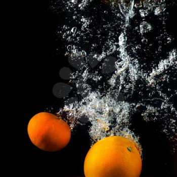 Fresh oranges falling into the water with a splash and air bubbles. Healthy food on black background. Wash fruits.