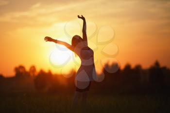 Woman with arms raised against the sunset background. Focus on model. Shallow depth of field.